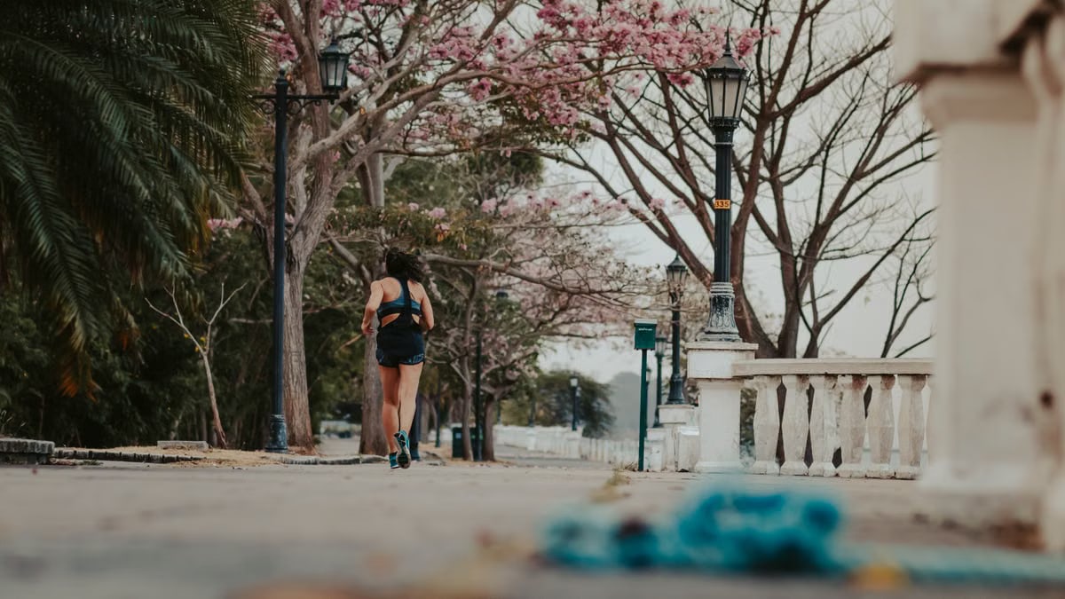 A woman jogs through a picturesque park lined with blooming spring trees and vintage lamps.